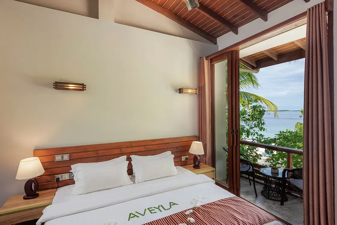 Ocean Deluxe room at Aveyla Manta Village with a timber headboard and balcony doors opening onto palms and the lagoon